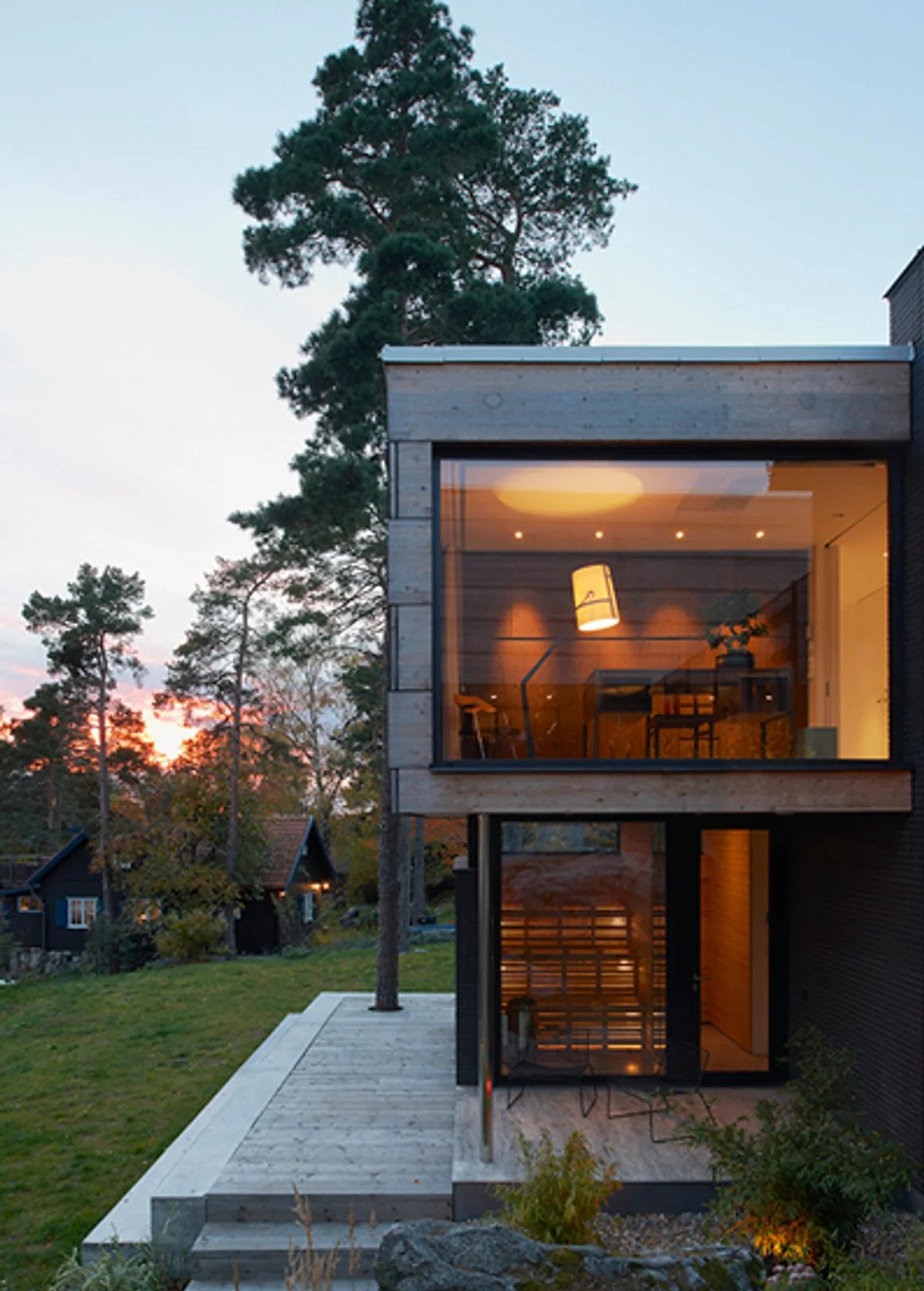 Modern villa i skymningsljus med varmt upplysta fönster, byggd av Vera & Sixten